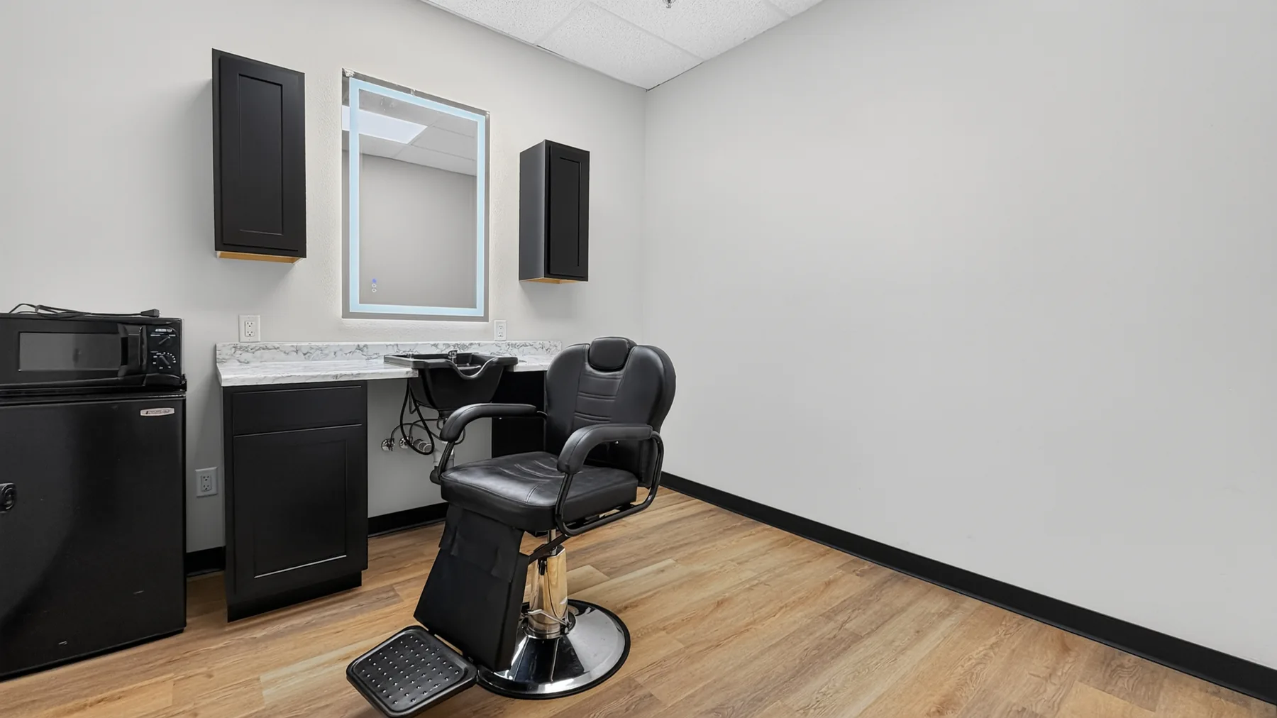 Private studio with styling chair, illuminated mirror, cabinets, and wash basin