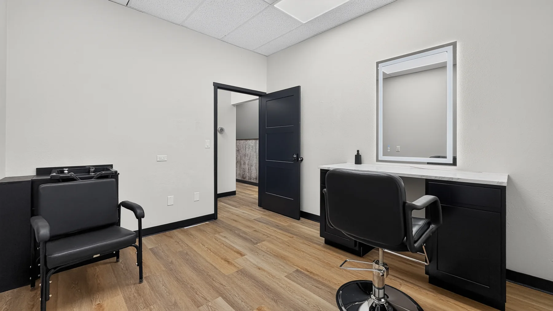 Furnished private suite with styling station, mirror, seating, and doorway to the hall