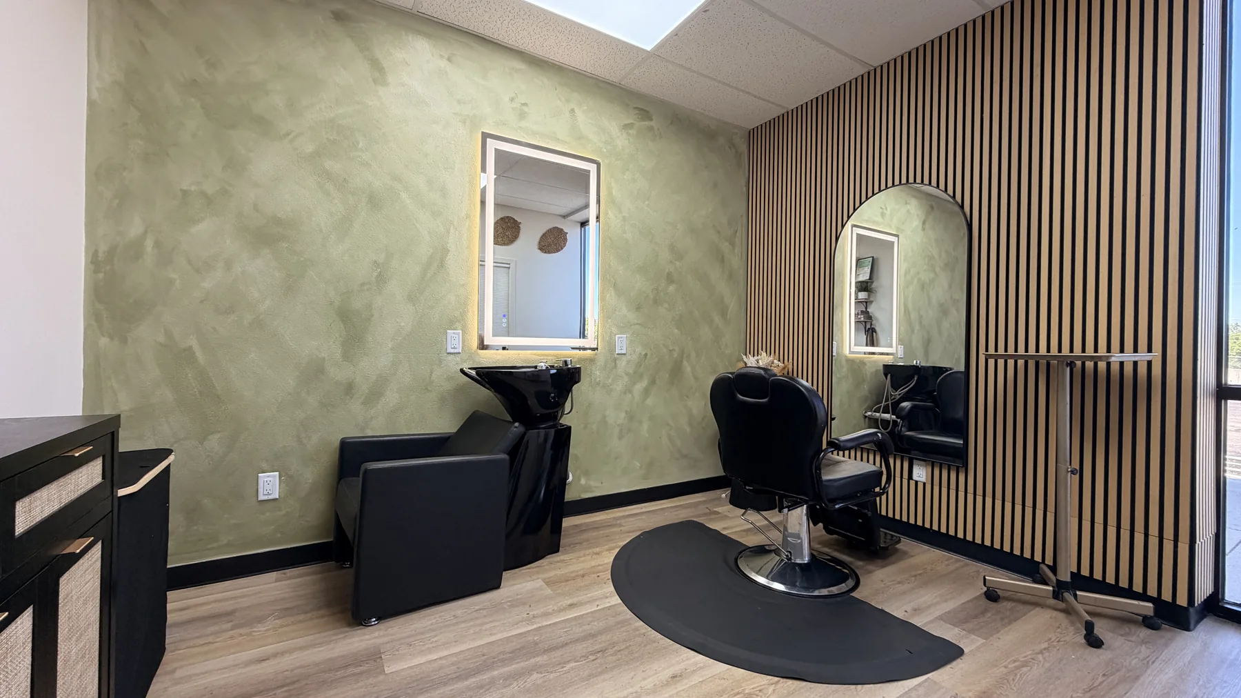 Customized suite with green textured walls, wood-slat accent wall, styling chair, mirrors, and wash station