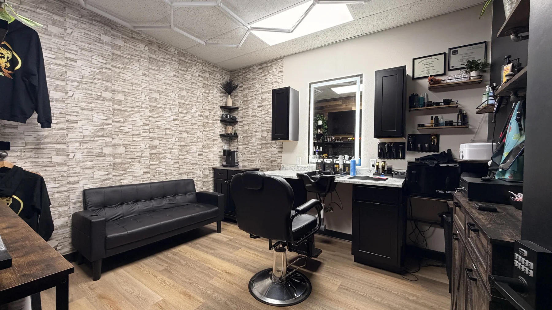 Customized barber and styling suite with a stone-look wall, sofa, illuminated mirror, cabinetry, and product shelves